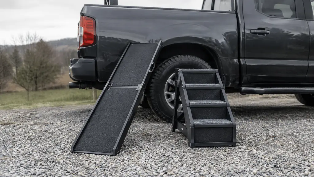A folding dog ramp and a set of folding dog stairs placed side by side on a gravel driveway.